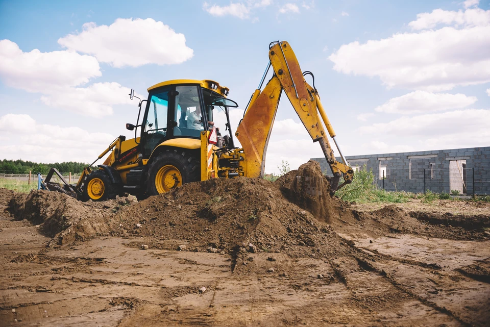 Excavateur travaillant sur le chantier de construction de maison - creusant les fondations d'une maison moderne