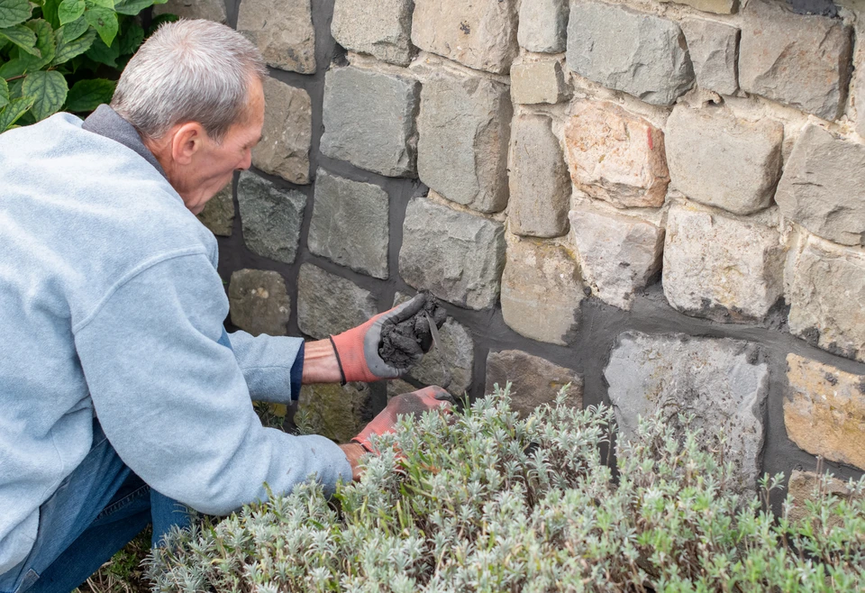 Ouvrier en b&acirc;timent construisant un mur de briques rouges en ext&eacute;rieur sous ciel bleu