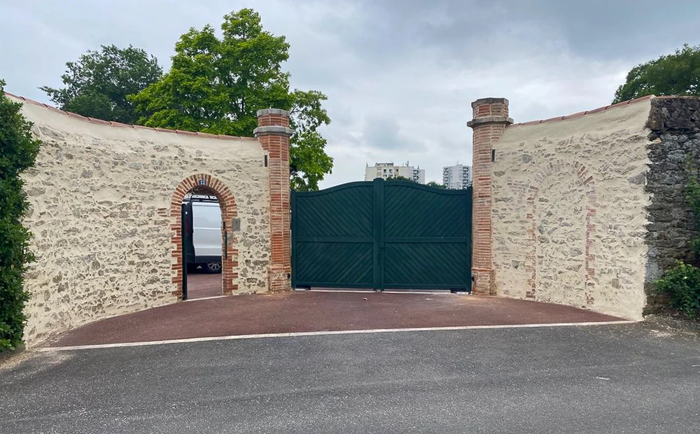 Façade en pierre traditionnelle avec fenêtres à encadrement brique rouge, végétation grimpante sur appuis
